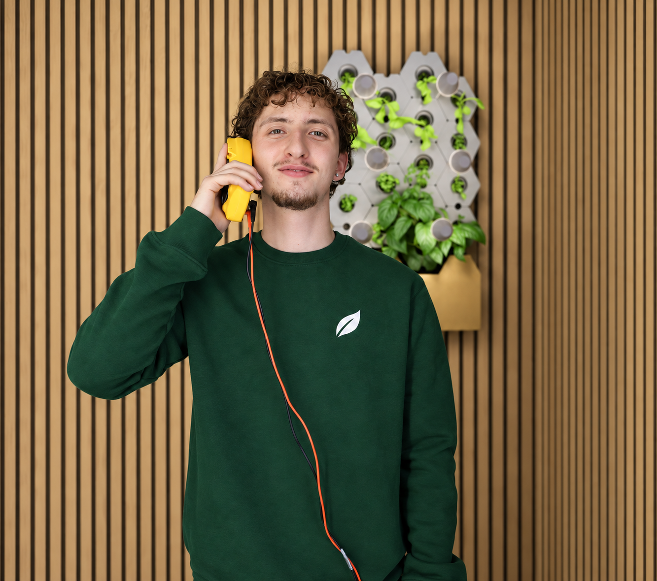 Nick von CompactGreens berät am gelben Telefon vor einer Pflanzenwand